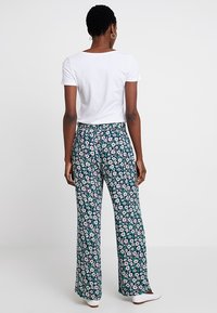 Rozszerzane spodnie w ciemnoniebieskim materiale z kwiatowym wzorem, zdobione różowymi i białymi kwiatami, zestawione z gładką białą koszulką.