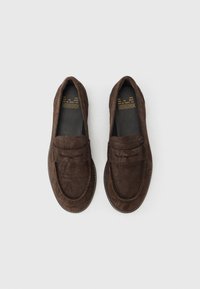 Καφέ μοκασίνια από σουέντ με σχέδιο ραφής, τετράγωνη μύτη και απαλή υφή. Διαθέτουν επίπεδη σόλα και ανοιχτό σχέδιο slip-on.