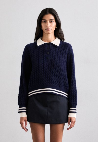 Pull en maille bleu marine avec un motif de câbles texturé, col blanc et ourlet en côtes rayées. Quatre boutons noirs à l'avant améliorent le design.