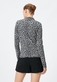 Maglietta a maniche lunghe in tessuto grigio con motivo maculato nero. Presenta un design aderente e una texture liscia. Abbinata a pantaloni corti neri.