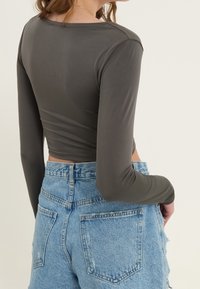 Graues langärmliges Crop-Top aus glattem Material, kombiniert mit hellblauen, hoch taillierten, ausgefransten Denim-Shorts.