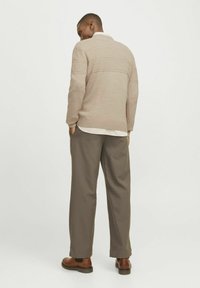 Pull en maille beige à rayures texturées, associé à un pantalon gris et des bottes en cuir marron. Le col et les poignets sont à rayures blanches.