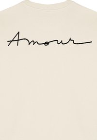 Krém színű pulóver, fekete hímzett "Amour" felirattal a hátsó részen. Puha tapintású, klasszikus kerek nyakú kialakítású.