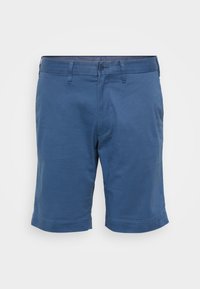 Kes Pendek sedang dalam kapas biru padat. Memiliki penutupan butang, gelung tali pinggang, dan hem yang digulung. Tekstur yang halus, tanpa corak atau aksen yang terlihat.