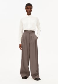 Camicia bianca a maniche lunghe con colletto, abbinata a pantaloni grigi a vita alta e morbidi, e scarpe nere testurizzate.