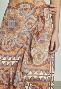 Jupe orange à motifs ornée de motifs paisley complexes en bleu et marron, en tissu léger, avec un drapé fluide et un détail latéral.