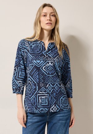 Chemise bleu marine avec des motifs géométriques complexes dans des nuances de bleu, dotée d'un col en V et de manches trois-quarts.