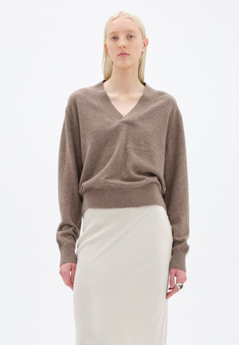 Maglione marrone a collo a V in un morbido tessuto a maglia, abbinato a una gonna liscia di colore chiaro. Maniche lunghe con vestibilità rilassata e fondo a costine.
