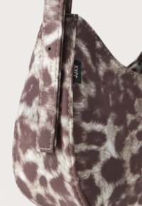 Torba za roko z rjavim in belim vzorcem tie-dye, z všitim trakom in majhno črno tkanino etiketo na strani.