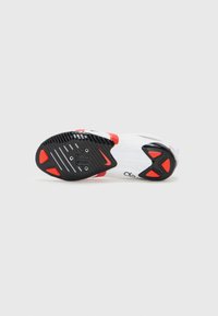Chaussure de cyclisme blanche avec des accents noirs et rouges. Présente une semelle en caoutchouc noir texturé avec des points d'attache pour les cales et des évents de drainage.