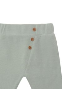 Hellgrüne Baumwollleggings mit einer strukturierten Oberfläche, elastischem Bund und drei braunen Knöpfen auf der linken Seite.