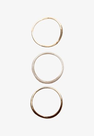 Kolme metallirenkaat pinottuna pystysuoraan: ylin on kiiltävää kultaa, keskellä harjattua hopeaa, alhaalla kiillotettua kultaa. Kaikki renkaat ovat pyöreitä ja sileitä.