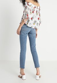 Vit off-shoulder blus med blommönster, med volangärmar. Pudrad med ljusblå denimjeans och vita klacksandaler.