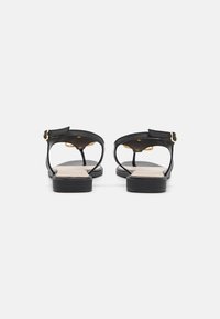 Sandali neri in pelle con un design minimale, caratterizzati da una suola piatta, un retro aperto e un dettaglio in oro sulla cinghia alla caviglia.