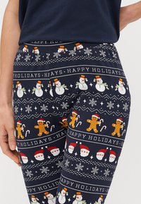 Leggings en color navy con un diseño navideño que incluye muñecos de nieve, muñecos de jengibre, caras de Santa y copos de nieve. Cintura elástica, material suave y elástico.