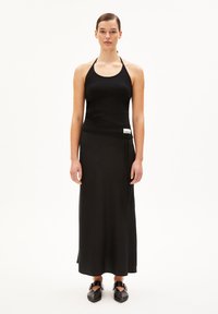 Zwarte geribbelde haltertop gecombineerd met een vloerlange zwarte rok, met een strikdetail en een klein merketiket op de taille. Zwarte schoenen maken de look compleet.
