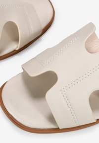White leather sandals feature a cutout design with open sides, contrasting stitching, and a natural rubber sole. Simple and practical shape.