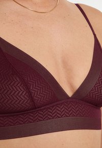 Bralette en bourgogne profond, présentant un design en V, un motif tricoté texturé et une large bande de soutien, avec des bretelles fines et réglables.