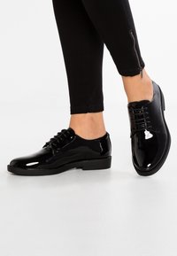 Chaussures à lacets en cuir verni noir avec un bout arrondi, un petit talon et une texture lisse. Présente des lacets noirs et un subtil détail de couture.