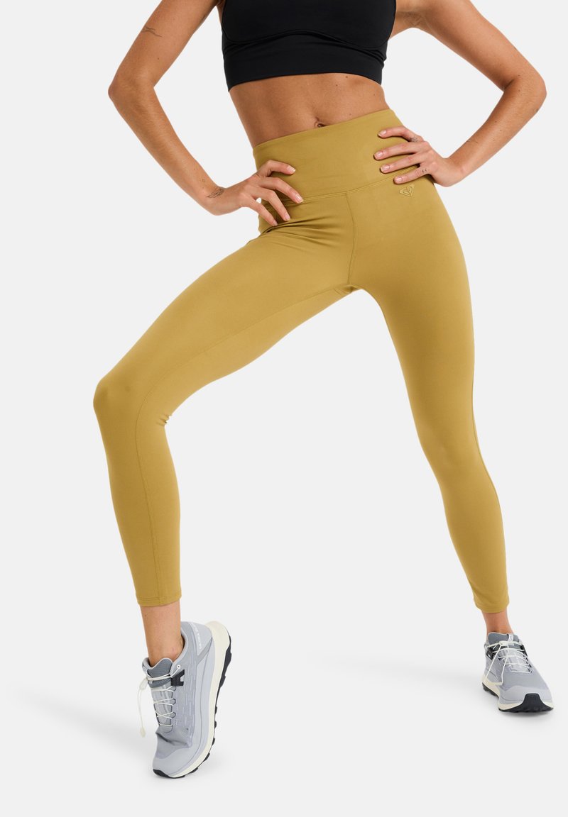 Leggings jaunes taille haute au design sans couture et en tissu extensible, associés à des chaussures de sport grises avec une semelle texturée et des lacets.