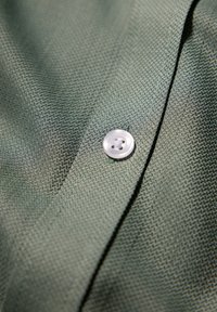 Primo piano di un tessuto verde texture con un bottone bianco a quattro fori cucito vicino a una cucitura.