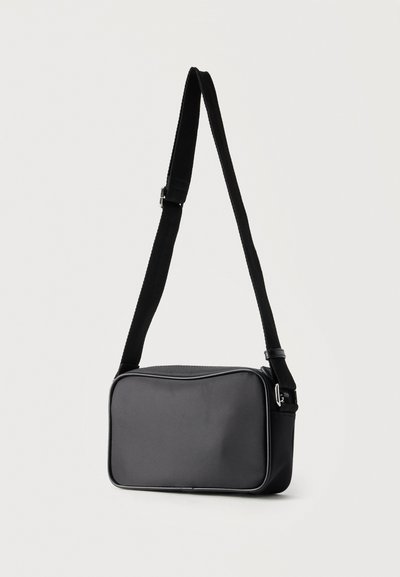 Μαύρη ορθογώνια τσάντα χιαστί με ρυθμιζόμενο λουράκι και ασημένια αγκράφα σε απλό φωτεινό φόντο.