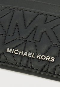 Čierna kožená peňaženka s reliéfnym geometrickým vzorom a výrazným strieborným logom "MICHAEL KORS". Hladká textúra s kontrastným prešitím.