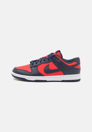 Sneaker navy e rossa con tomaia in pelle, punta perforata, suola intermedia bianca e suola esterna in gomma. Presenta il classico logo Nike sul lato.