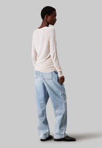 Maglione lavorato a maglia crema con maniche lunghe, abbinato a jeans blu chiaro larghi. L'outfit presenta una vestibilità rilassata e polsini a coste.