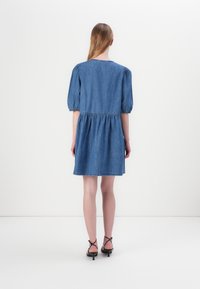 Denimkjole med innsvingt midje og puffede korte ermer, med en samlet skjørt og en rund halslinning. Farge: mellomblå.
