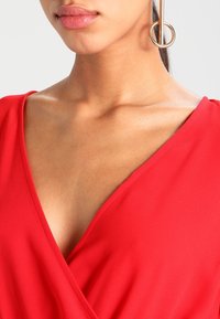 Vestido rojo envolvente con un escote en V profundo, tejido suave y mangas cortas. Presenta un diseño en capas y sutiles detalles de costura.