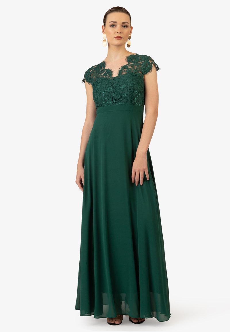 Lungo abito verde con corpetto in pizzo, maniche a sbuffo e una gonna fluente. Tessuto liscio con una leggera lucentezza, pizzo dettagliato attorno al collo.