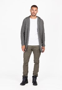 Cardigan grigio, texture a rilievo con cappuccio, indossato sopra una camicia bianca. Pantaloni cargo oliva con tasche laterali e stivali neri stringati.