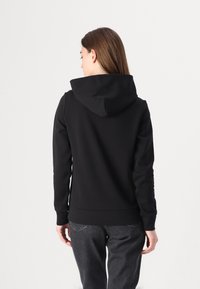 Sweatshirt à capuche noir avec une texture douce, un design ajusté et un ourlet côtelé, associé à un pantalon gris foncé.
