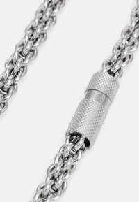 Silver chain necklace with interlinked metal links. Features a textured cylindrical clasp with "GUESS" engraved. Smooth and shiny finish.