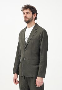 Giacca di lino verde oliva con due bottoni, rever a taglio e una tasca sul petto. Design casual con una vestibilità rilassata e dettagli di cucitura visibili.