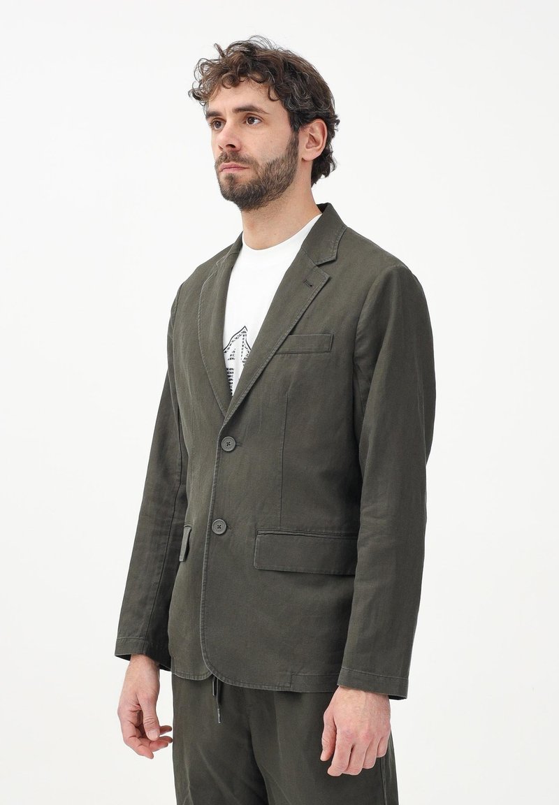 Giacca di lino verde oliva con due bottoni, rever a taglio e una tasca sul petto. Design casual con una vestibilità rilassata e dettagli di cucitura visibili.