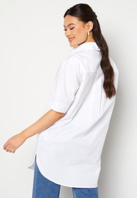 Camicia bianca con maniche corte, caratterizzata da un colletto e un orlo curvo. Tessuto morbido con una vestibilità comoda.