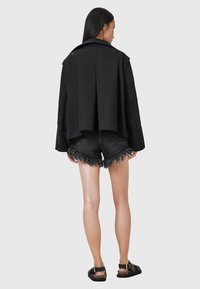 Giacca nera oversize con retro corto, abbinata a pantaloncini di jeans neri strappati. La modella indossa sandali neri.