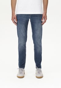 Slim-Fit blaue Jeans mit einer ausgewaschenen Optik, subtilem Used-Look und klassischem Fünf-Taschen-Design, kombiniert mit hellgrauen Sneakers.