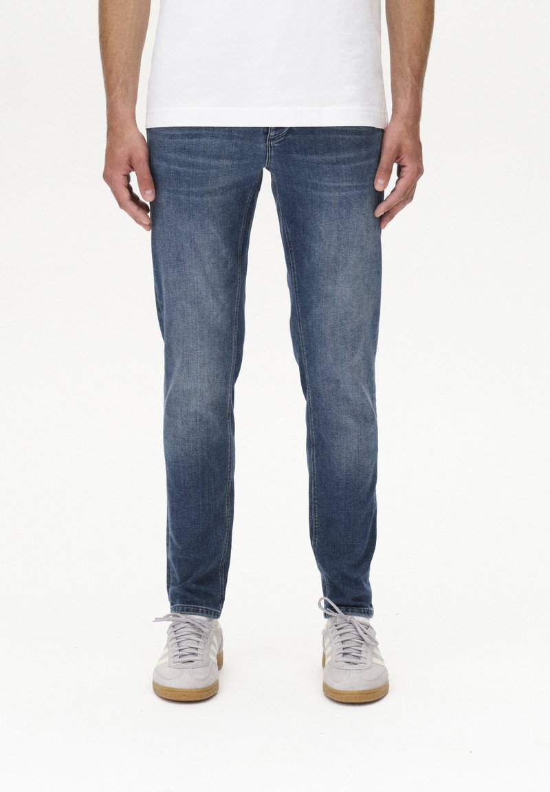 Slim-Fit blaue Jeans mit einer ausgewaschenen Optik, subtilem Used-Look und klassischem Fünf-Taschen-Design, kombiniert mit hellgrauen Sneakers.