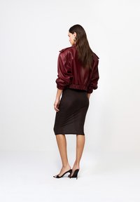 Burgundská kožená bomber bunda s elastickým lemom a rukávmi, spárovaná s priliehavou hnedou ceruzkovou sukňou a čiernymi stiletto podpätkami.