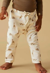 Pantalon en coton blanc avec cordon de serrage, arborant un motif animalier avec des girafes, des léopards et des éléphants. Texture douce avec un détail bouton.
