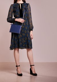 Długa sukienka z długim rękawem w ciemnoniebieskim kolorze, ozdobiona motywem kwiatowym i falbankami przy dekolcie. Do kompletu czarne, platformowe buty z ćwiekami oraz niebieska torebka.