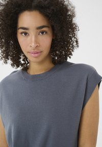Grå ærmeløs bluse lavet af blødt stof, med en rund halsudskæring og ribbede detaljer ved skuldrene. Glat tekstur med et minimalistisk design.