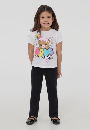 Maglietta bianca con un orsetto dei cartoni animati e palloncini, stampata con testo multicolore. Abbinata a pantaloni neri e scarpe nere lucide.