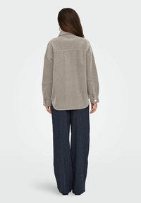 Chemise en velours côtelé gris clair avec col, coupe décontractée, poignets à boutons et épaules tombantes. Assotie avec un pantalon large rayé bleu marine.
