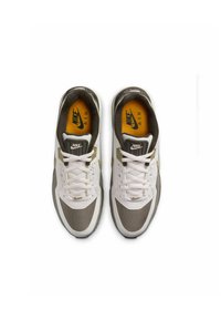 Las zapatillas Nike Air en blanco y gris cuentan con una parte superior de malla, un cuello acolchado y plantillas amarillas. La marca es visible en la lengüeta y los laterales.