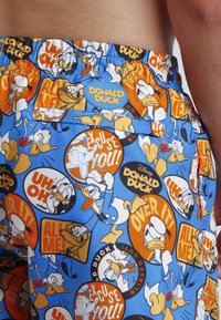 Pantalones cortos azules con un patrón repetido de ilustraciones de Pato Donald y frases de texto en naranja y negro; con cinturilla elástica y bolsillo lateral.