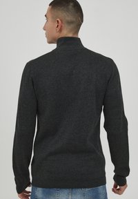 Pulover gri închis, cu mâneci lungi și guler înalt, realizat dintr-un material neted. Prezintă manșete și tiv cu nervuri. Vedere din spate a puloverului.